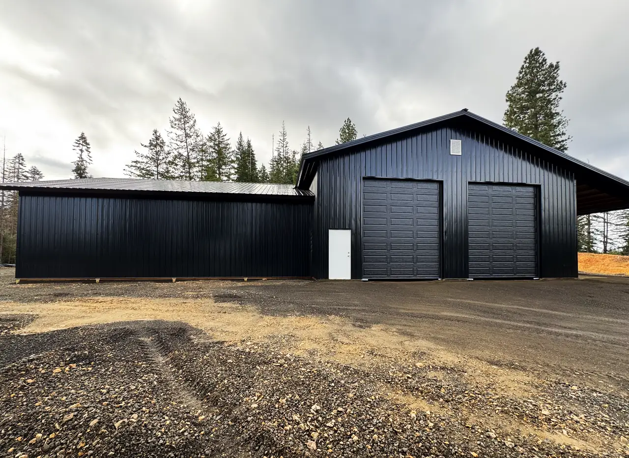 Finished black steel pole building with two overhead doors and an attached lean-to